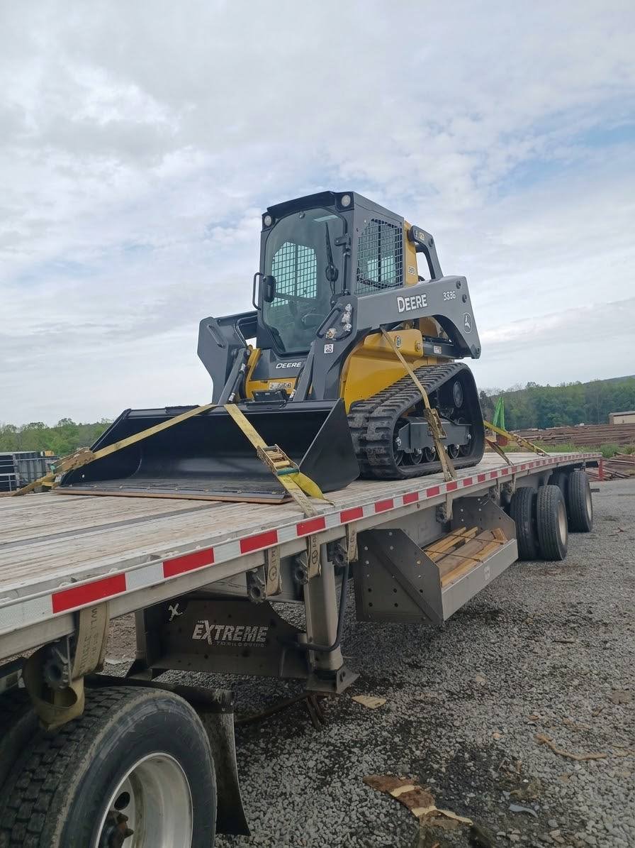 Compact track loader strapped down on a flatbed trailer, ready for delivery